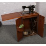 A Singer treadle sewing matching in walnut cabinet, with sewing lamp and other accessories.