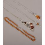 Three silver amber set pendants on chain along with an amber necklace.