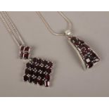Two silver and garnet set pendants on chain.