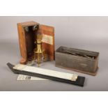 A cased J Swift & Son brass workshop microscope, along with a Thornton slide ruler and tin of tools.