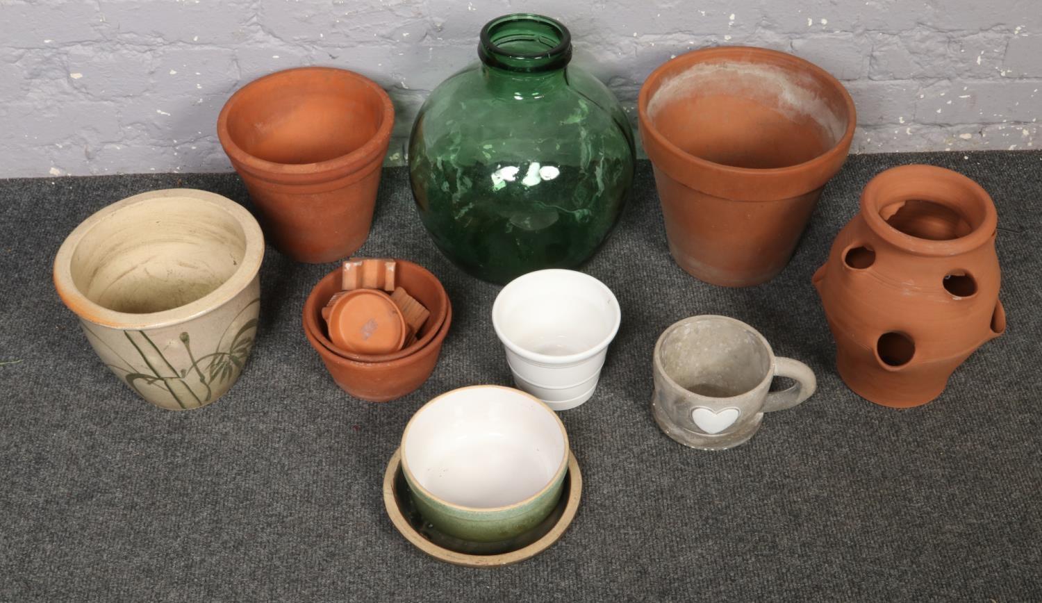 A quantity of terracotta garden planters along with a green glass carboy.