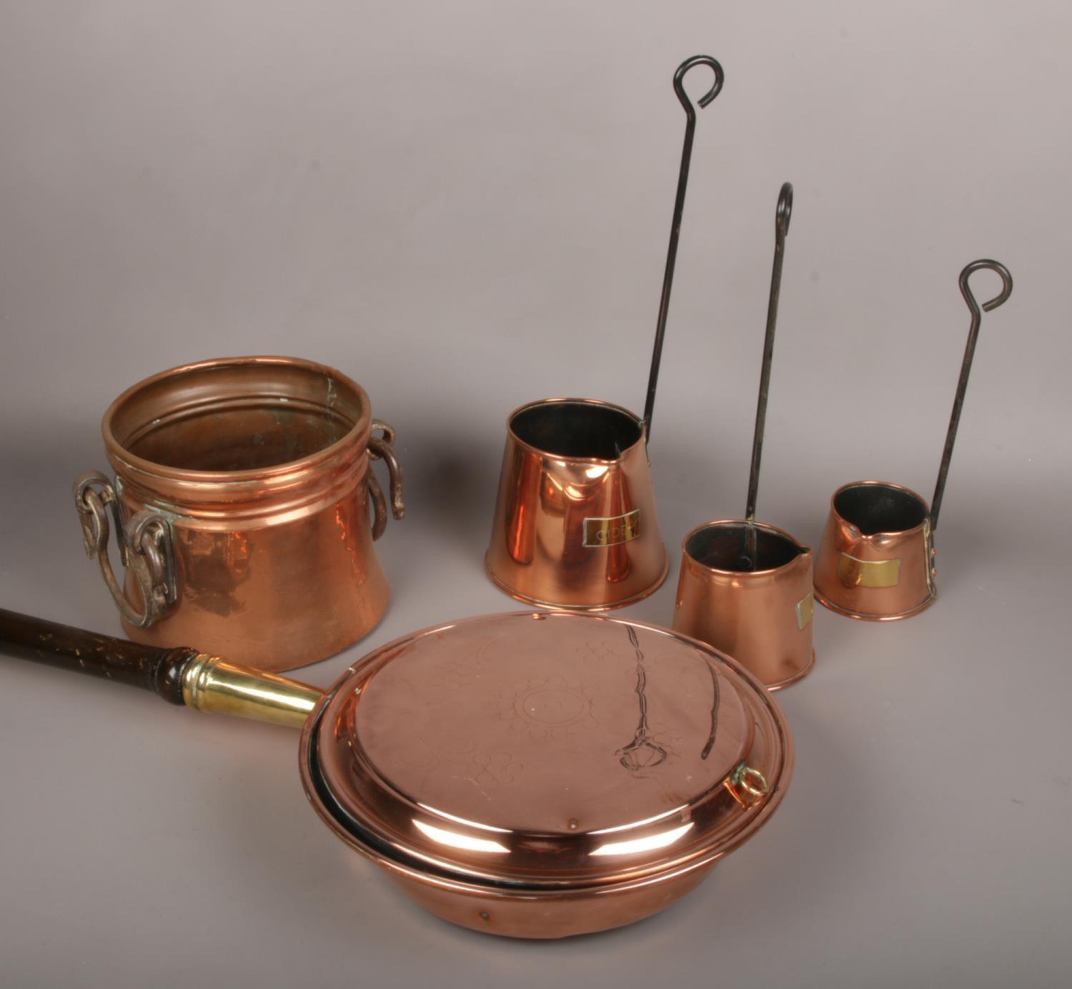 An antique copper planter with iron handles, three copper cider toddys and a copper bed warming pan.