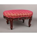 A carved mahogany footstool. with overstuffed top and raised on scroll supports, 35cm x 45cm.