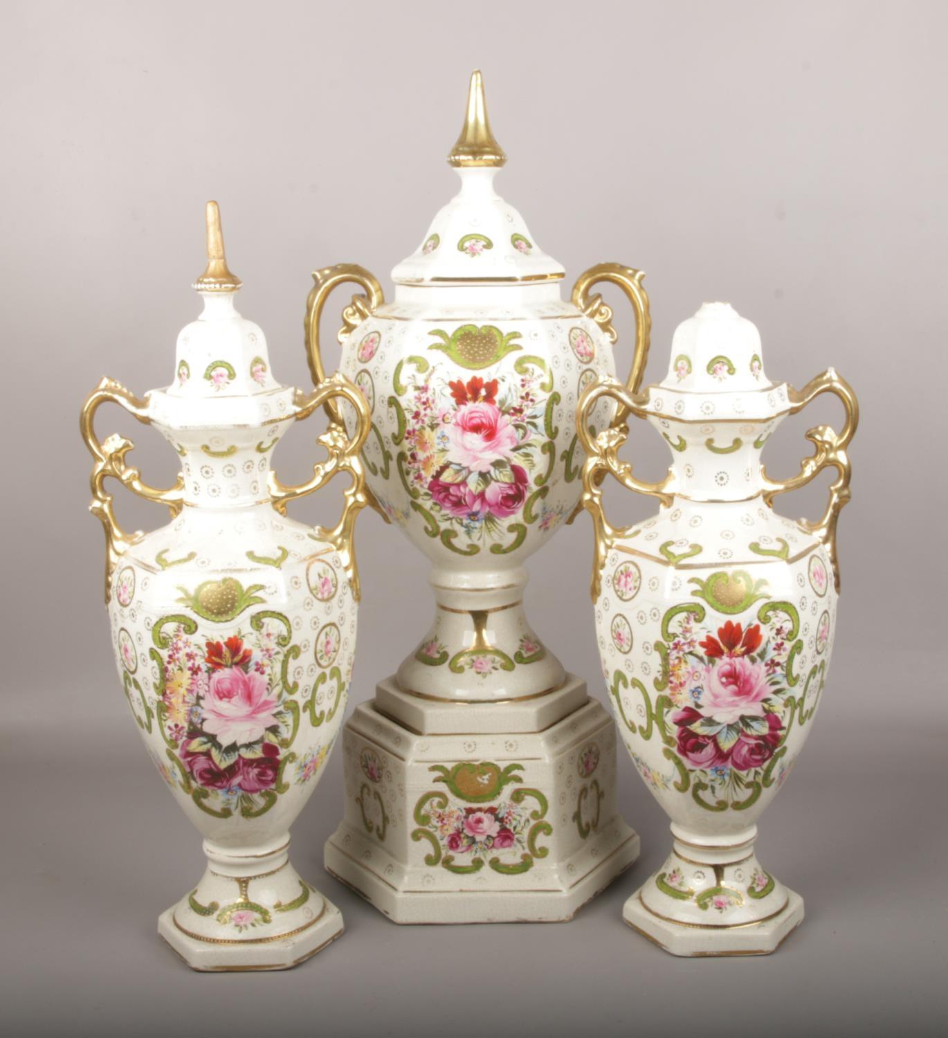 A pottery garniture, with gilt and floral decoration. Two finials repaired. Crack to lid. One finial
