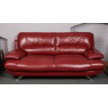 A modernist red leather and chrome three seater settee and armchair raised on splay supports.