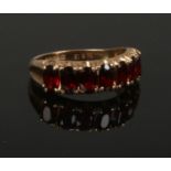 A 9ct gold seven stone garnet ring. Set with ovoid stones upon reeded shoulders, size M.