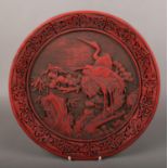 A Chinese cinnabar style dish. Decorated in relief with cranes in a landscape with pine trees.