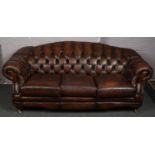 A large brown leather deep buttoned three seat sofa.