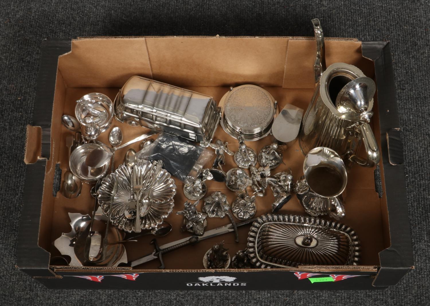 A box of silver plate, coffee pot, jug, fairy figurines, cutlery, sugar tongs etc