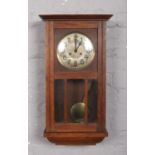 An oak cased wall clock with silvered dial and Arabic numeral markers.