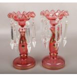 A pair of red coloured glass lustres with gilt decoration. Repair to one.