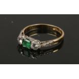 An 18ct gold and platinum three stone emerald and diamond ring. With a square cut emerald flanked by