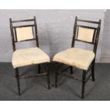 A pair of ebonised dining chairs with cream upholstery.