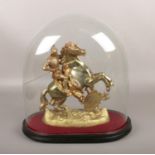 A gilt metal figure of a knight on horseback, under Victorian glass dome.
