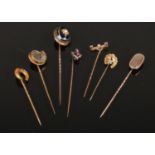 Seven antique yellow metal stick pins with assorted terminals. Including ammonite fossil, banded