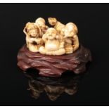 A Japanese Meiji period carved ivory large netsuke on carved hardwood plinth. Formed as a group of