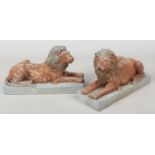 A pair of painted composite models of recumbent lions raised on rectangular plinths, 34.5cm long.