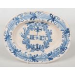A 19th century oval Continental delft marriage dish. Painted with a cross and initials under a