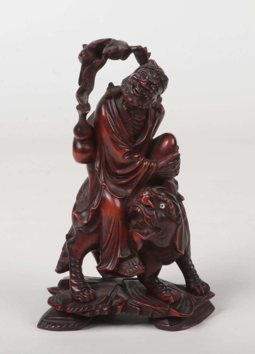 A 19th century Chinese carved wood figure of a man mounted upon a lion dog. With glass inset eyes