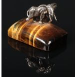A tigers eye paperweight surmounted by a white metal model of an elephant, 5cm high. Good
