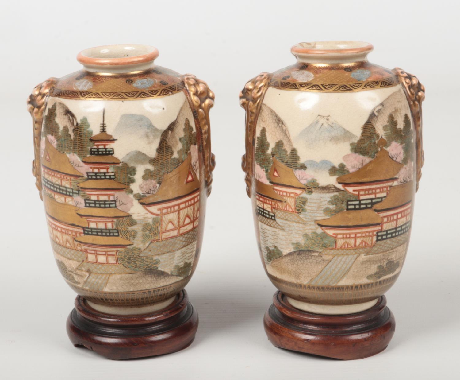 A pair of Japanese Meiji period Satsuma vases on hardwood plinths. Each with moulded mask handles