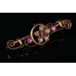 A 15 carat gold ruby and diamond bar brooch. Of open scrollwork form and with floriform centre, 42mm