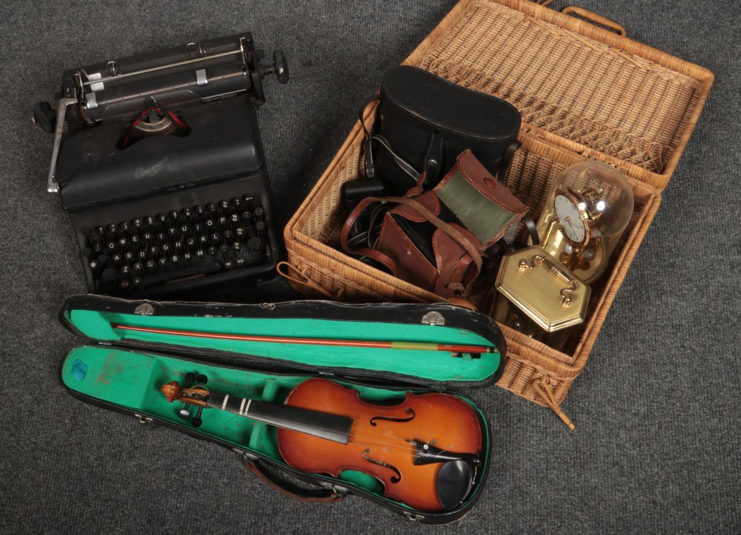 A wicker basket with contents of clocks, cameras, cased Lark violin, typewriter etc.