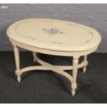 A painted oval coffee table decorated with flowers and having x-frame cross stretcher.