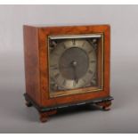 A burr walnut cased mantel clock. With brass square dial ornamented with spandrels and marked Made
