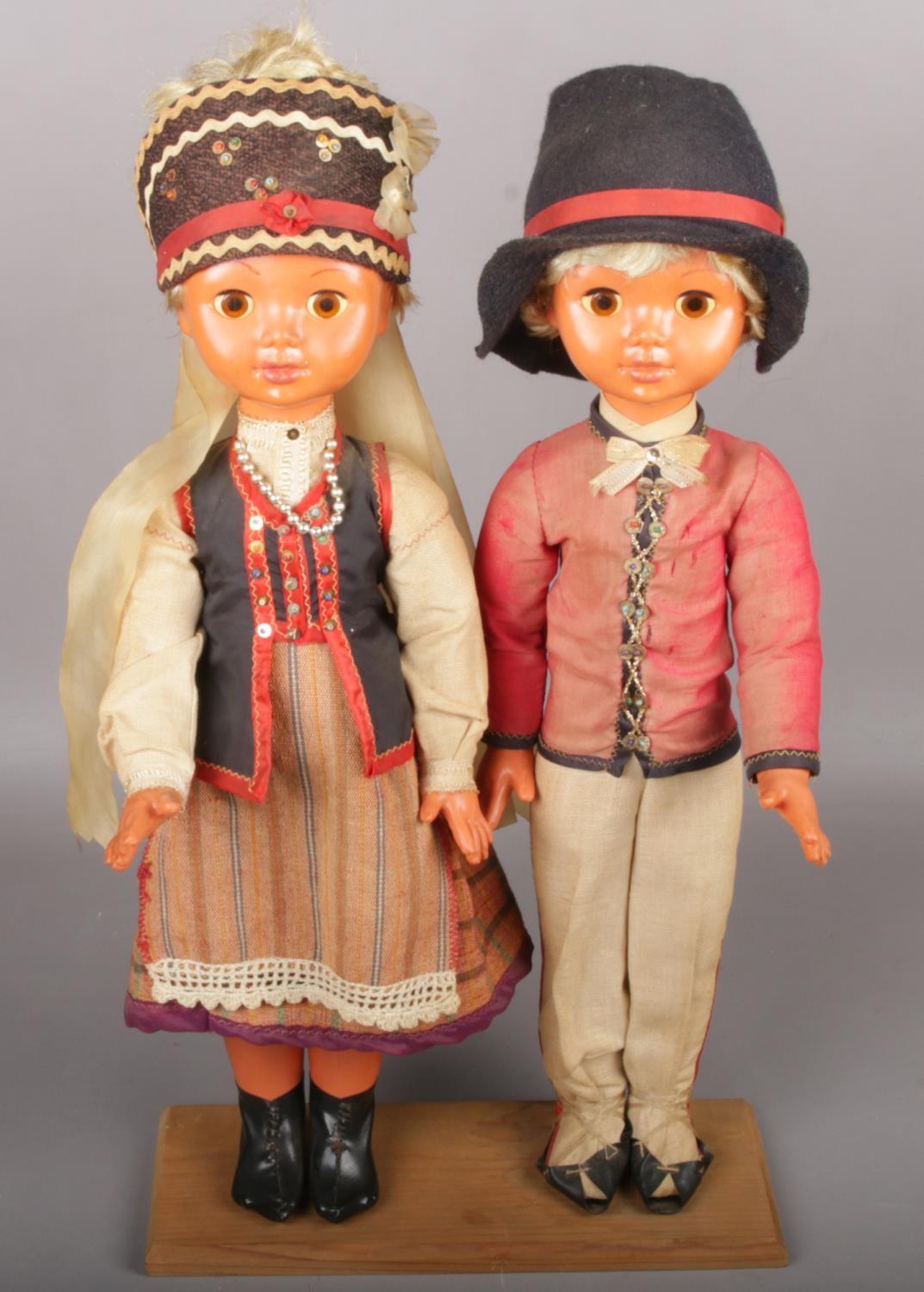 A pair of European dolls raised on wooden plinth.