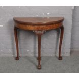 A Queen Anne style figured walnut demi lune fold over card table. Raised on acanthus carved cabriole