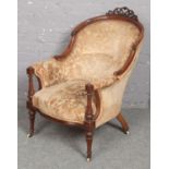 A Victorian carved walnut upholstered tub chair. With open scroll work cresting rail and raised on