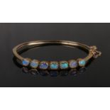 A 9ct gold bangle set with seven opals. Each stone housed within a lobed frame, 10.9 grams, 62mm