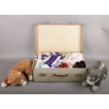 A vintage suitcase containing vintage dolls clothing along with a TY cat and rabbit.