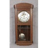 An oak cased wall clock with silvered dial and Arabic numeral markers. Top side of clock in need