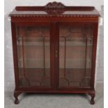 A astragal glazed mahogany display cabinet with carved gallery, raised on ball and ball feet.
