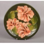 A Moorcroft plate, in the Hibiscus design on green ground. (Diameter 26cm). Good condition.