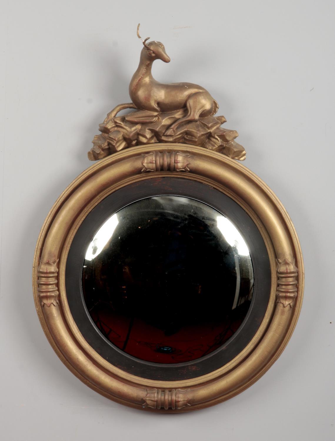 A Regency gilt framed convex circular wall mirror, the pediment formed as a recumbent deer, 90cm x