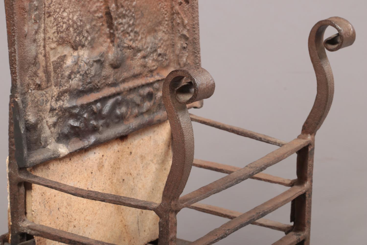 An 18th century wrought iron fire grate. The arch top back decorated in relief with a figure and - Image 2 of 8