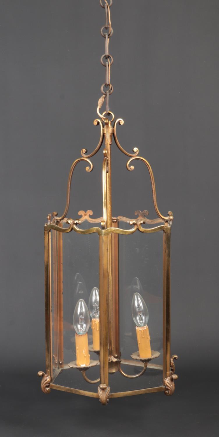 A hexagonal brass and glass three branch hall lantern. With double scrolling pediment and cast