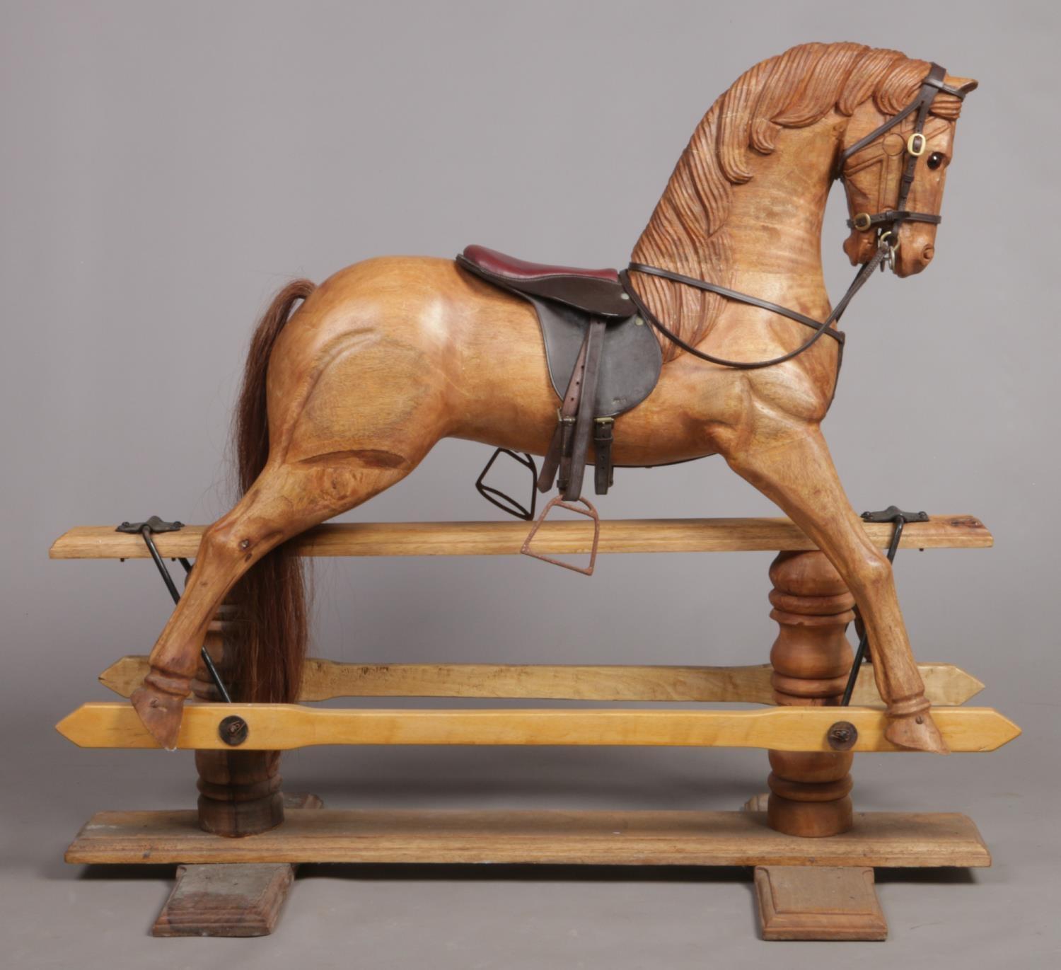 A large carved hardwood child's rocking horse with leather saddle and bridle, 105cm high. Stripped