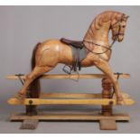 A large carved hardwood child's rocking horse with leather saddle and bridle, 105cm high. Stripped