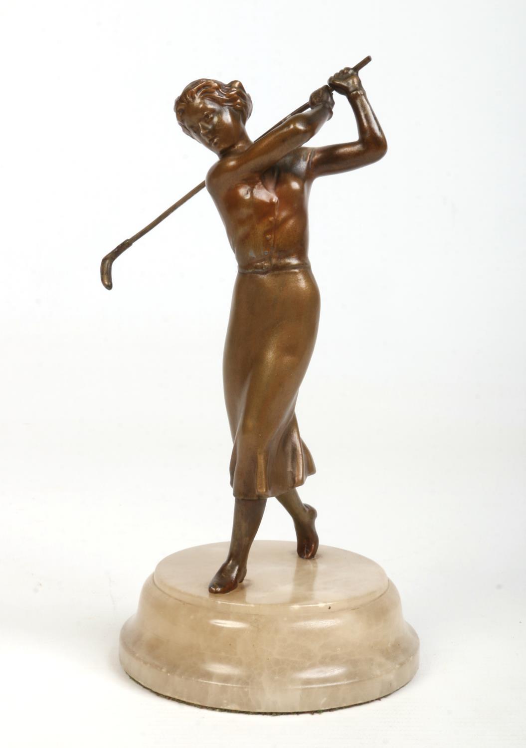 An Art Deco cold painted spelter figure formed as a female golfer mid swing and raised on an