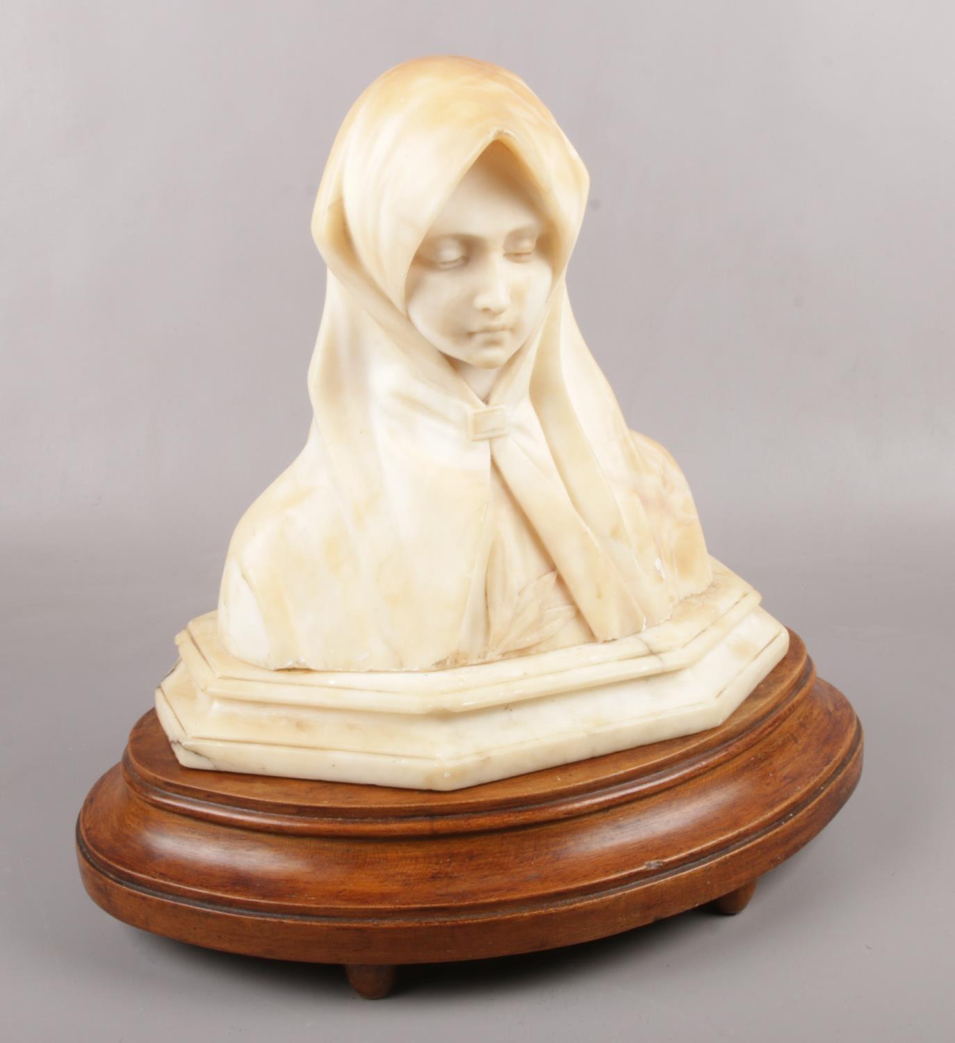 An alabaster bust of the Virgin Mary, raised on wooden plinth. (Total height 38cm).