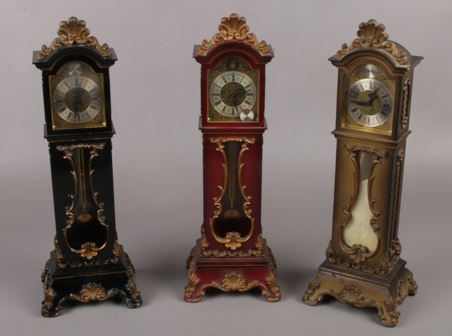 Three miniature grandfather alarm clocks. (33cm high) Hinge on black clock broken. Catch on back
