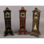 Three miniature grandfather alarm clocks. (33cm high) Hinge on black clock broken. Catch on back