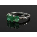 A white metal three stone emerald ring, with diamond set shoulders.