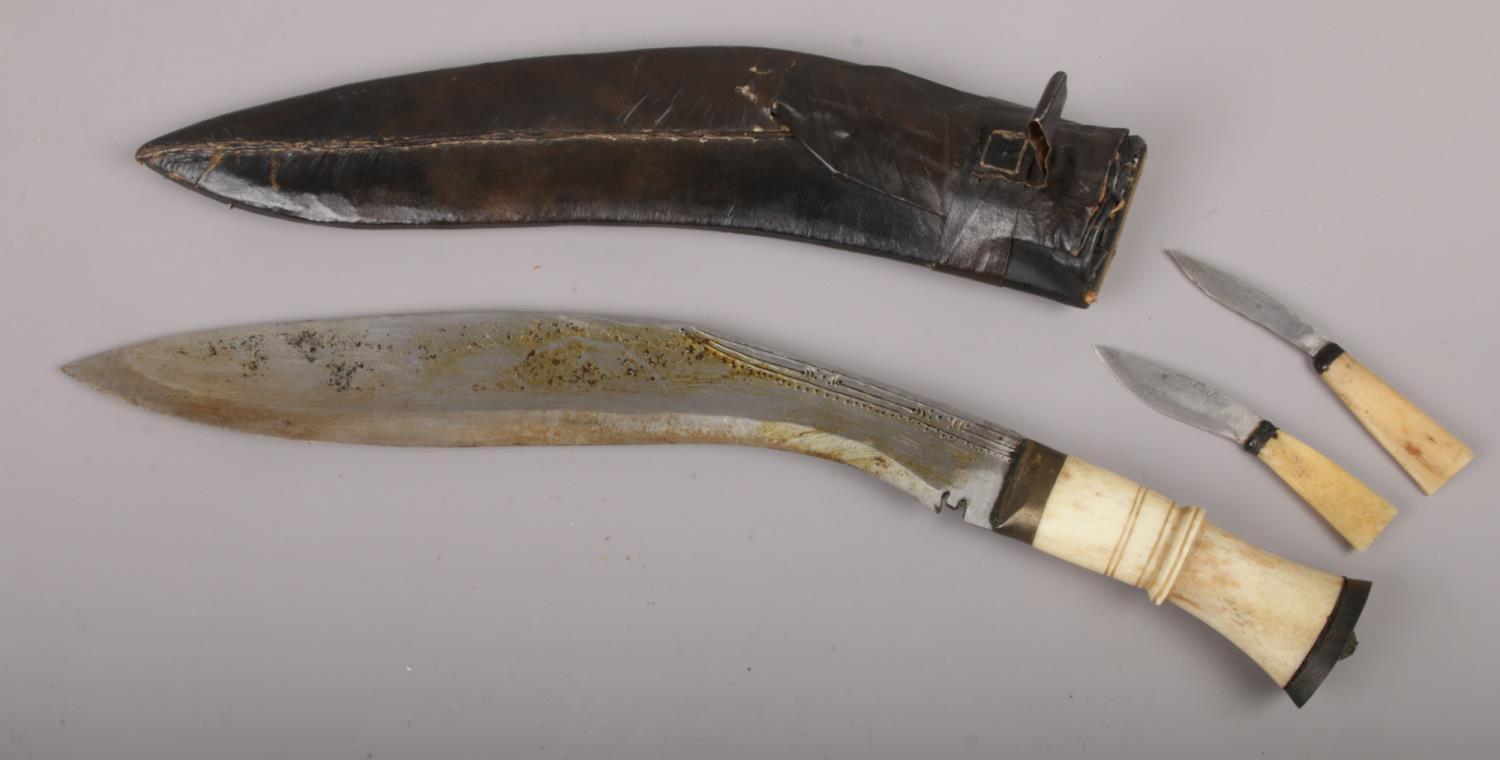 A gurkha's kukri knife in scabbard with carved bone grip and two smaller accompanying knives.