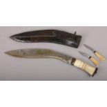 A gurkha's kukri knife in scabbard with carved bone grip and two smaller accompanying knives.