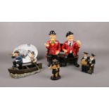 A group of Laurel & Hardy ceramic figures, in a rowing boat, sat on a bench, sat on suitcase